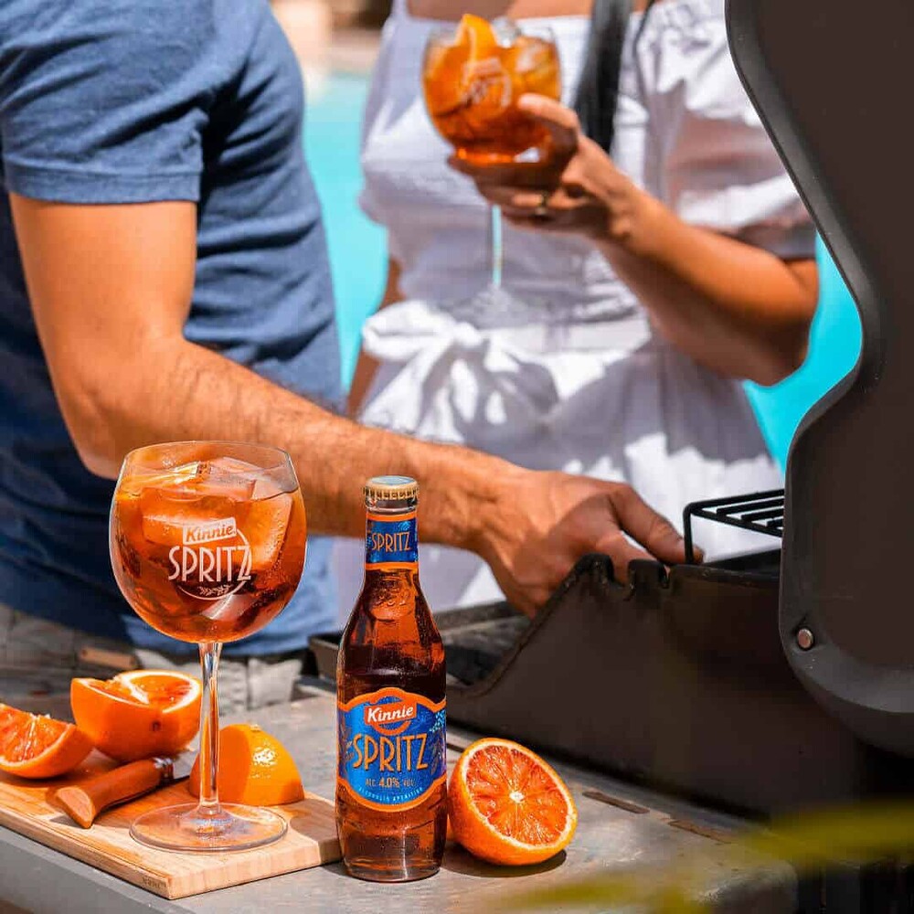 Kinnie Spritz Flasche und gefülltes Glas mit Orangen am Pool beim Grillen