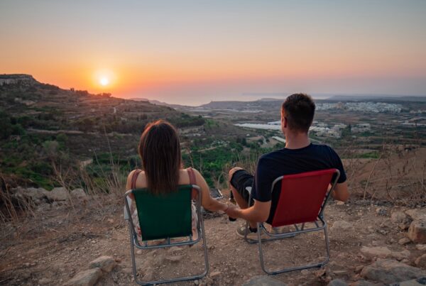 Paar in Campingstühlen blickt auf den Sonnenuntergang über der maltesischen Landschaft