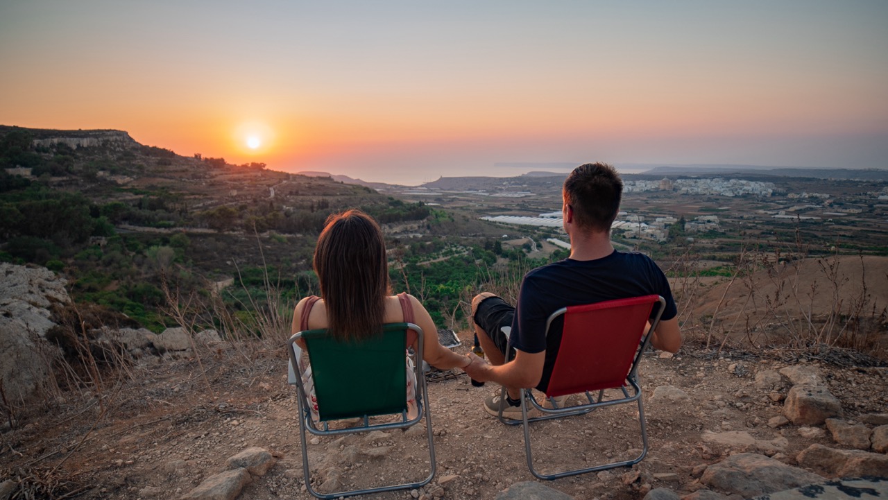 Paar in Campingstühlen blickt auf den Sonnenuntergang über der maltesischen Landschaft