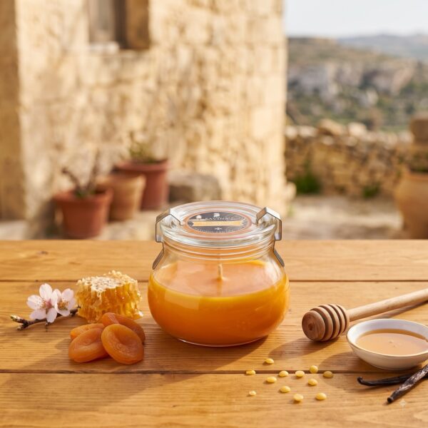Orangefarbene Duftkerze Honig im Bügelglas mit Honigwabe und Honiglöffel