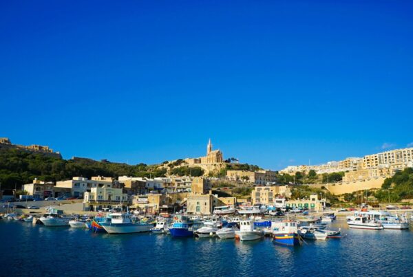 Hafen von Mġarr auf Gozo mit bunten Fischerbooten und Kirche am Hang