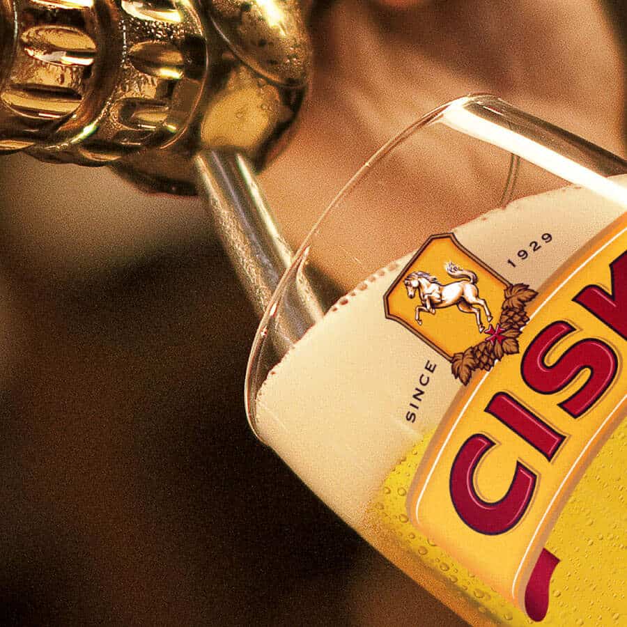 Cisk Lager wird aus der Flasche in ein Glas mit Cisk-Logo eingeschenkt