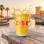 Cisk Lager in der 330-ml-Dose am Strand von Malta mit Luzzu-Booten im Hintergrund