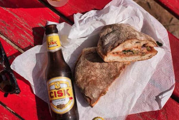 Cisk Lager Flasche und Glas neben einer maltesischen Ftira auf rotem Holztisch