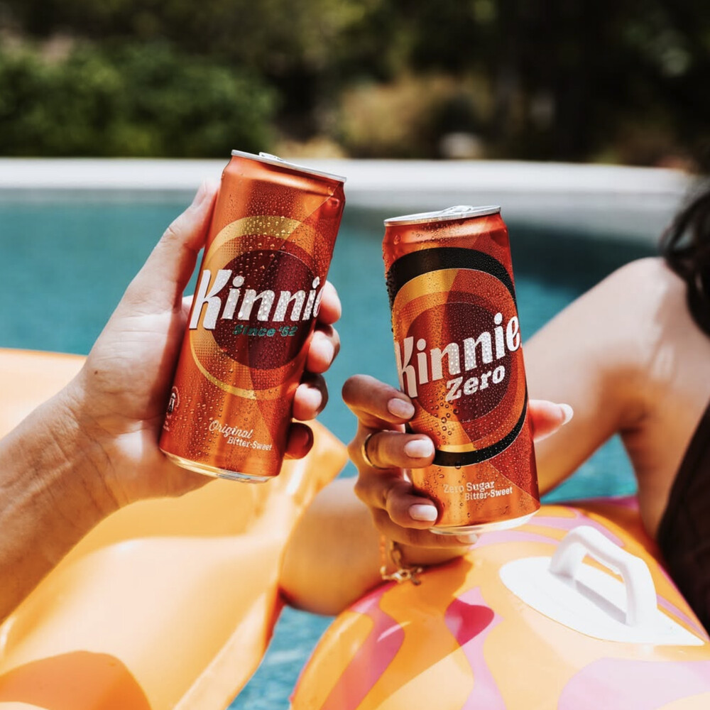 Zwei Hände stoßen mit Kinnie Classic und Kinnie Zero Dosen am Pool an