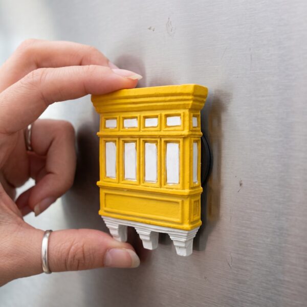 Kühlschrankmagnet in Form eines gelben maltesischen Holzbalkons, in der Hand gehalten
