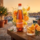 Kinnie Classic Flasche mit gefuelltem Glas vor einem maltesischen Hafen