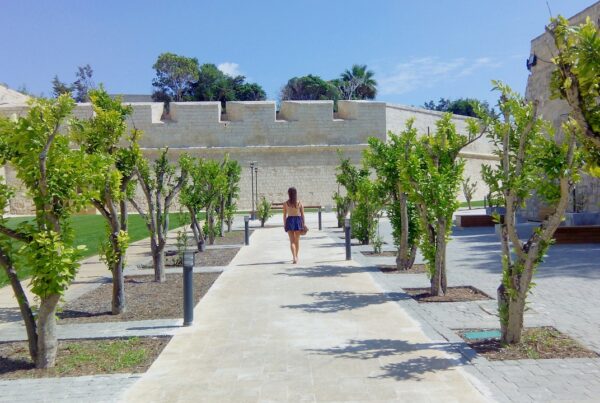 Frau spaziert durch den begrünten Wallgraben an der Stadtmauer von Mdina