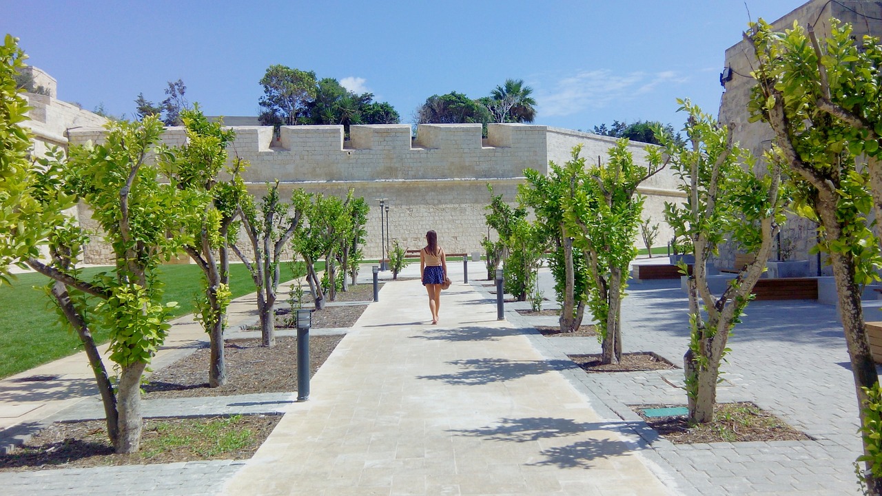 Frau spaziert durch den begrünten Wallgraben an der Stadtmauer von Mdina
