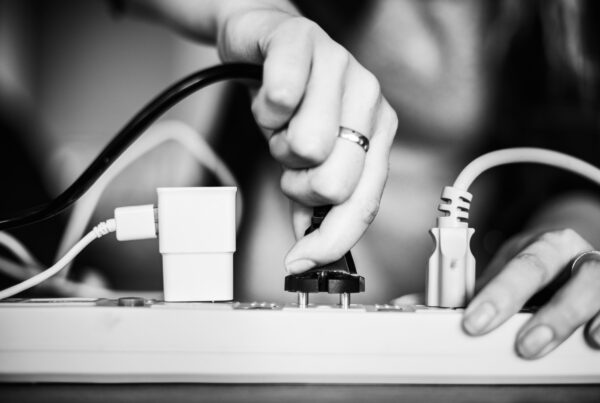 Hand steckt einen Netzstecker in eine Steckdosenleiste, Schwarz-Weiß-Aufnahme